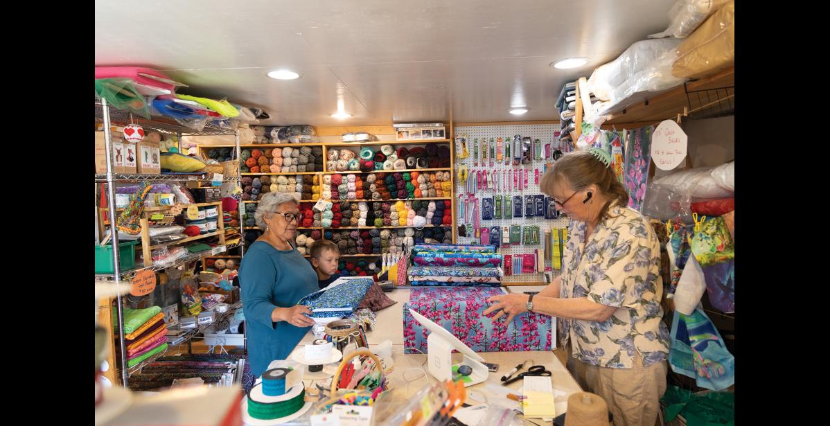Photo by Anna Lionas GOOD BYE–Josie Bourdon chats with Kirsten Bey, who measures and cuts fabric on Thursday July 31, the last day of Sew Far North under Bey’s ownership.