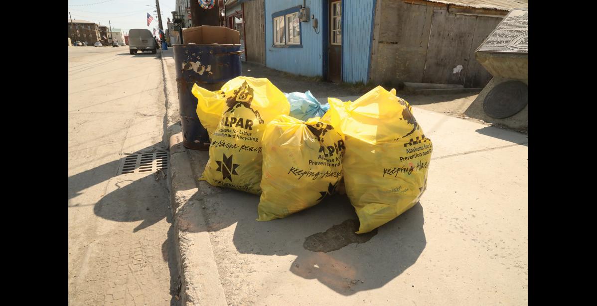 GARBAGE DAY—Three bright yellow trash bags wait on the curb on Front Street during Nome's spring cleanup week. Photo by Laura Robertson