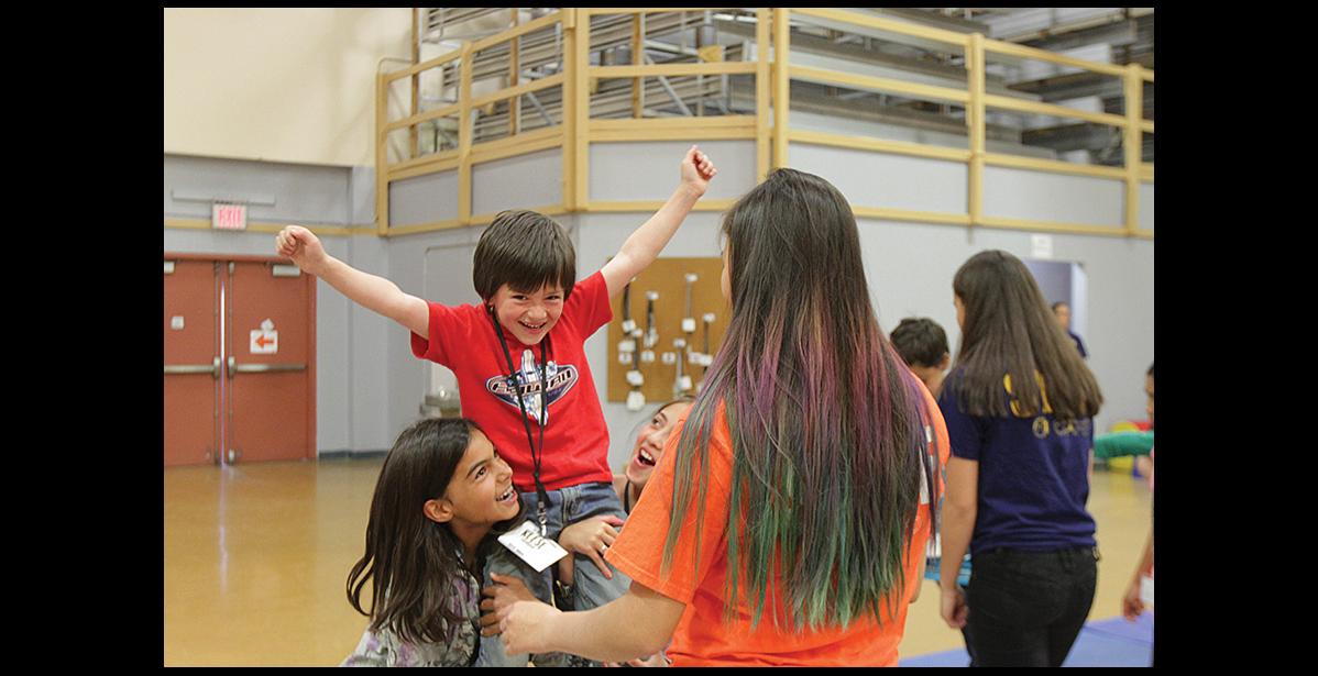 Photo by Maisie Thomas SUMMERCISE— Reese Knudsen, middle, and Ayla Trigg, left, are all smiles during CHEERios, a Summercise class, during which children learn the basics of cheerleading, including stunts, jumps, voice projection and safety.