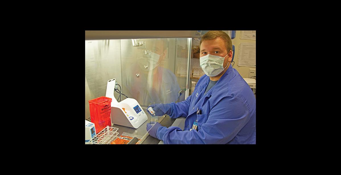 Photo courtesy NSHC/Reba Lean RAPID TESTING— Alex Bahnke, a general supervisor in the NSHC Laboratory, prepares to run a COVID-19 test on one of the new Abbott ID Now machines from under the safety of a fume hood in the Nome lab.