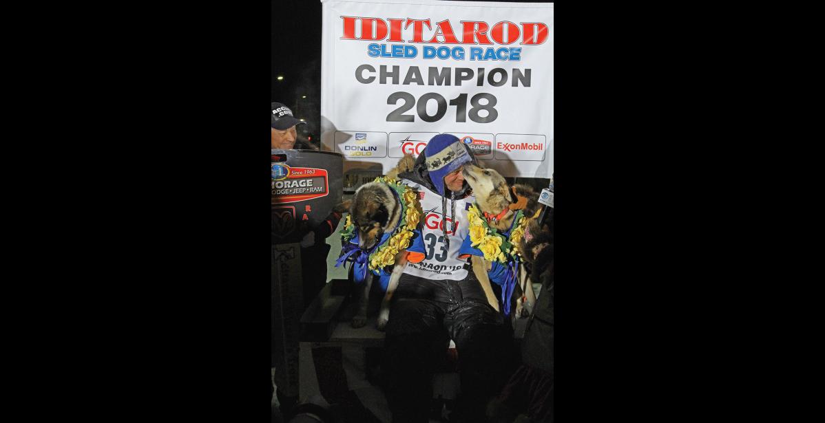 Photo by Diana Haecker 2018 CHAMPION— Joar Leifseth Ulsom of Norway won the Iditarod on March 14, 2018 at 3 a.m. At the champion podium he got a kiss from his lead dog Olive while holding his other lead dog Russeren.